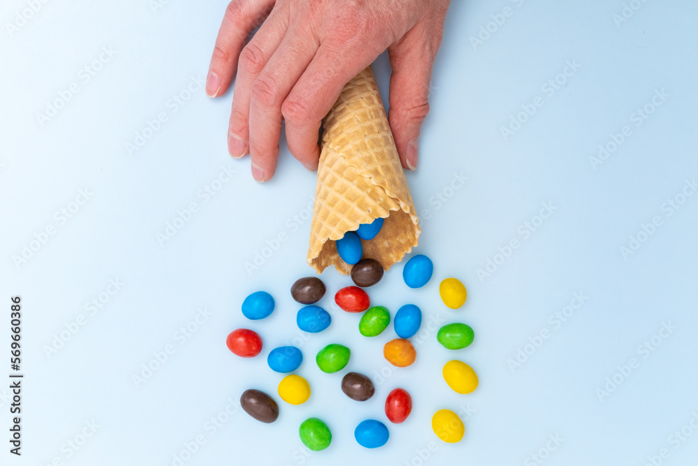 Obraz premium A hand holding an empty waffle cone with scattered multicolored round candies, dragees. A fun holiday