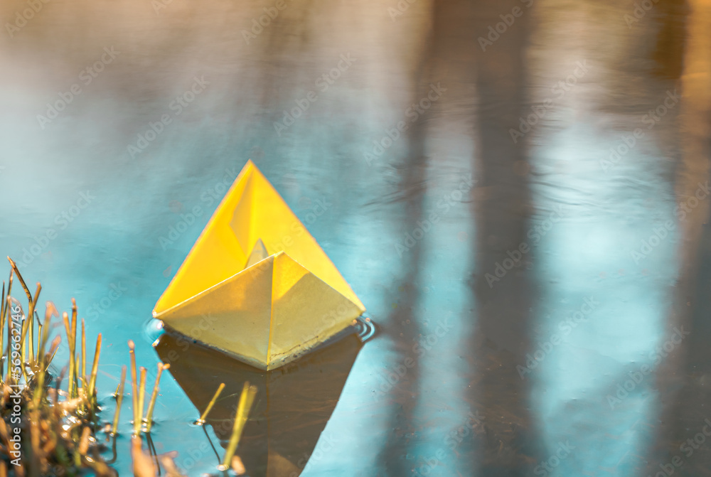 Yellow floating paper boat. Colorful sailing ship in big blue spring puddle, river water on winter street. Warm wet rainy weather, old grass. Hello spring, autumn. Children play, have fun outdoors