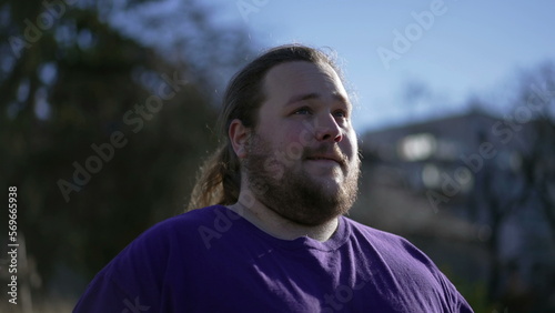 One pensive happy young man walking forward outside smiling. A joyful overweight guy walks outdoors feeling positive. Tracking shot