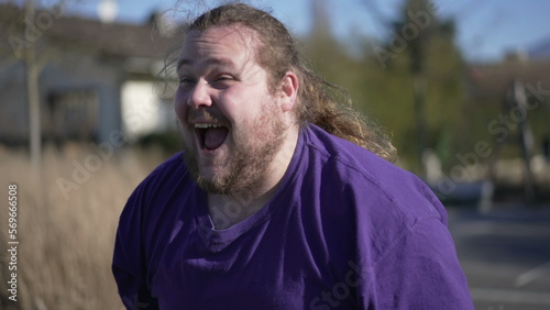 One happy overweight man walking forward outdoors smiling. A joyful fat guy portrait face close up in tracking shot