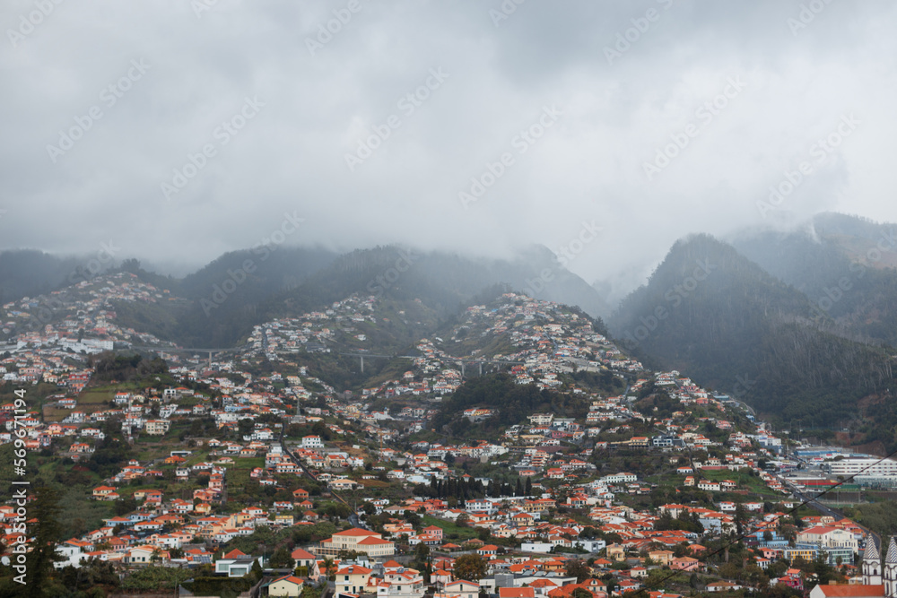 Beautiful green mountains with forest, houses and cloudy weather on the island of Madeira. Peaks and rocks in the clouds.
