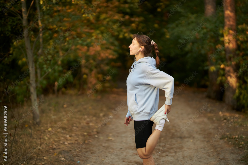 young beautiful girl sportswoman. girl athlete in a blue sweatshirt, goes in for sports. A young girl does morning exercises. Athletic young woman doing morning exercises in the park. 