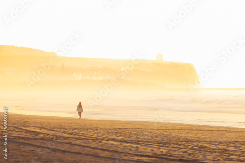 Woman walk on golden sand beach of portstewart strand by with castlerock lighthouse backgorund. Wild coast of northern ireland photo