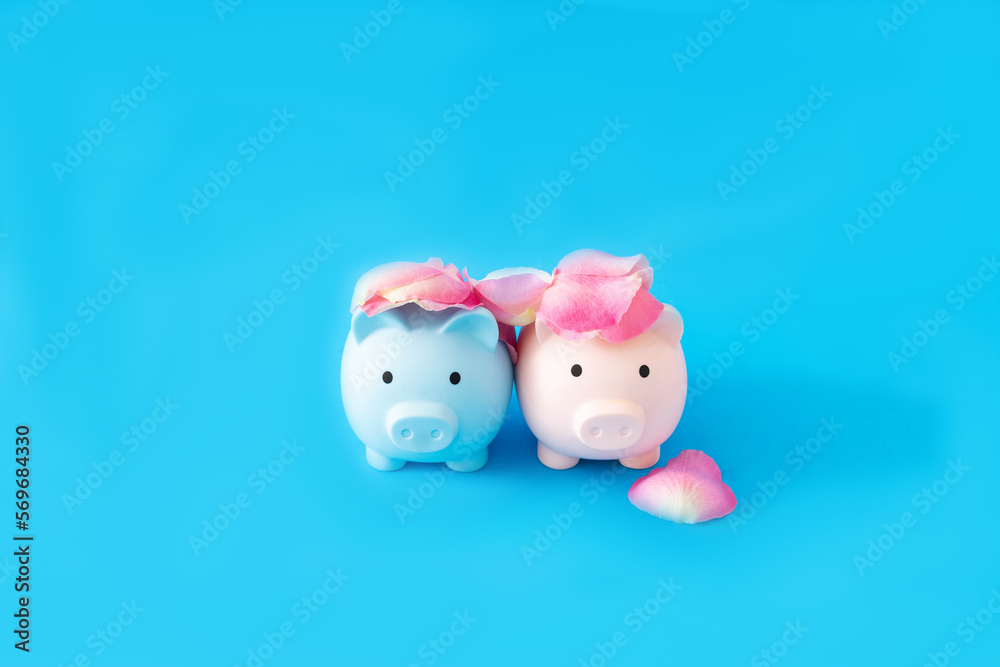 A blue and a pink piggy bank with rose petals on heads against blue background. Minimal surreal concept for Valentine or wedding card or banner. Design for editorial on love and money