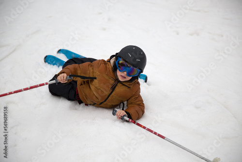 CLOSE UP: Boy falls on snow and slides towards camera while trying to ski.  Kids lands into snow after losing balance at ski down the slope at snowy ski resort.