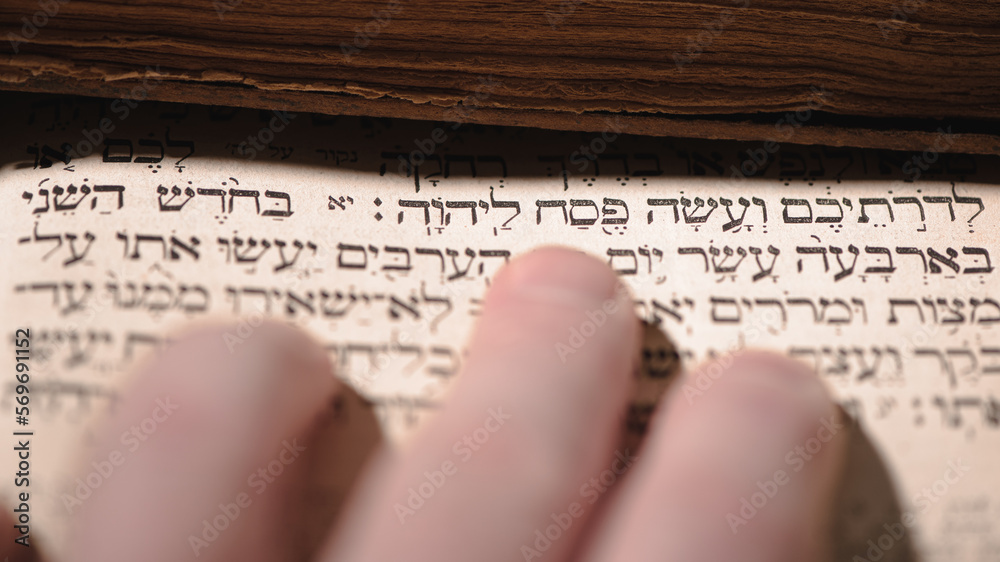 Fingers on page of old book Torah. Selective focus on snippet Hebrew Bible text that translates in english: offer the Passover sacrifice to Jehovah. Closeup.