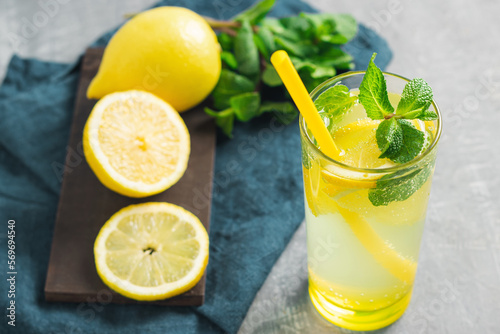 Lemonade drink or mojito cocktail in a glass with straw, lemon fruit and mint leaves, refreshing summer beverage