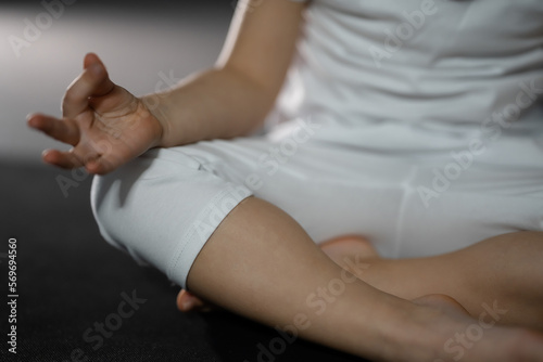 Three years old little girl meditating in a lotus pose on a gray background in dark room