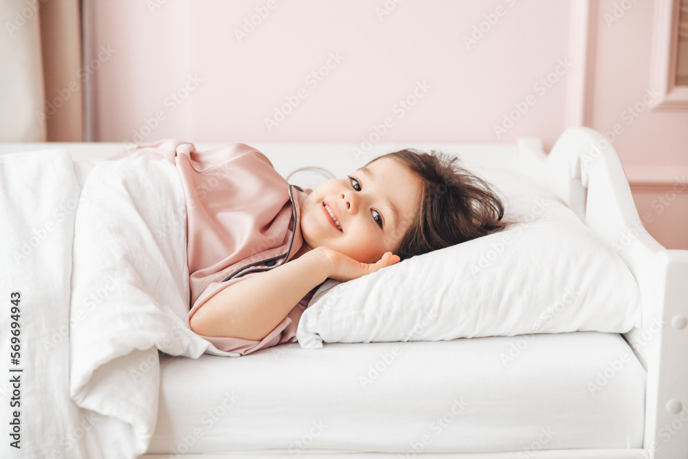 a little dark-haired girl, lying barefoot in bed. the child woke up after sleeping. good morning a little dark-haired girl, lying barefoot in bed. the child woke up after sleeping. good morning