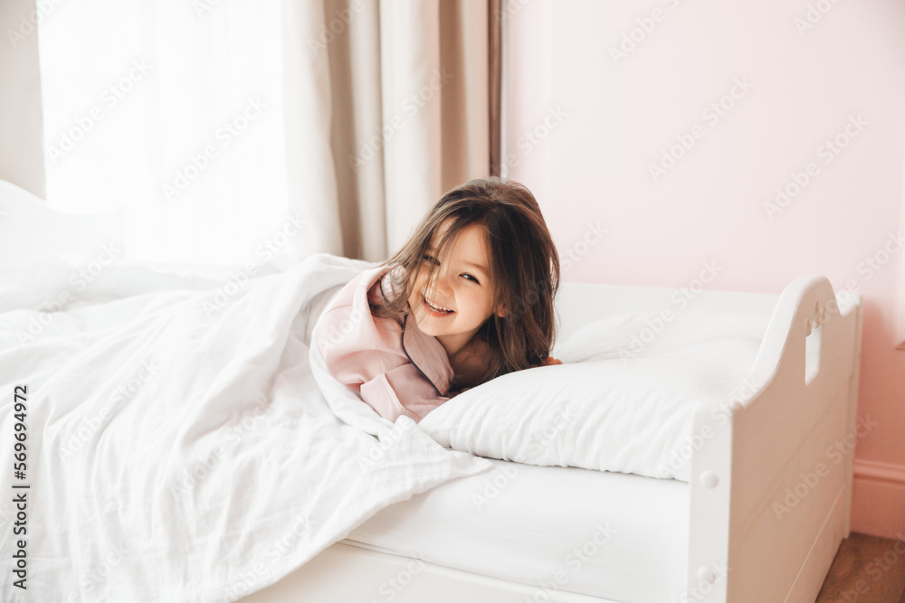 a little dark-haired girl, lying barefoot in bed. the child woke up after sleeping. good morning a little dark-haired girl, lying barefoot in bed. the child woke up after sleeping. good morning