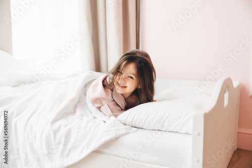 a little dark-haired girl, lying barefoot in bed. the child woke up after sleeping. good morning