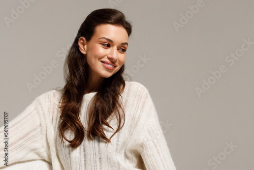 Happy young woman sitting on sofa at home and looking at camera. Portrait of comfortable woman in winter clothes relaxing on armchair. Portrait of beautiful girl smiling and relaxing during autumn.