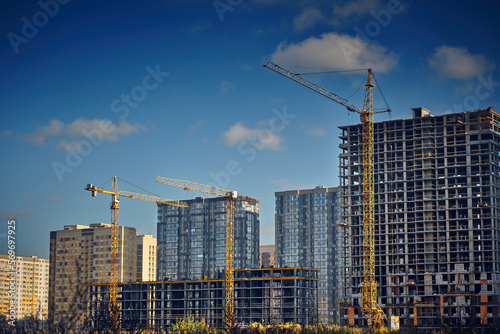 Group of tower cranes on the construction site against blue sky. Cranes for construction of high-rise buildings. Real estate construction. Concept of urban development and architecture.