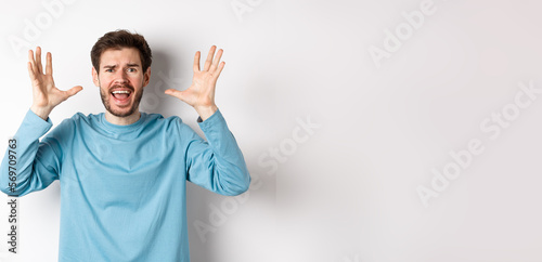 Image of freaked out young man screaming and shaking hands, shouting at camera frustrated or worried, panicking over white background photo