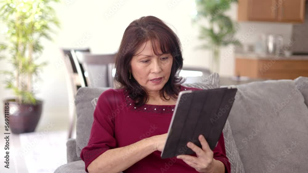 Beautiful middle age woman relaxing reading mobile tablet story peacefully sitting on comfortable couch in leisure home living room Beautiful middle age woman relaxing reading mobile tablet story peacefully sitting on comfortable couch in leisure home living room