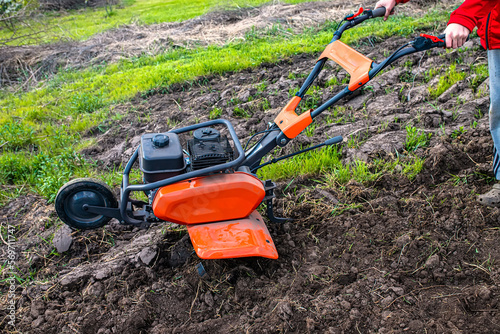 Orange professional cultivator or tiller on untreated soil before plowing. Treatment of virgin land before planting seedlings. photo