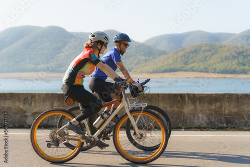 Asian cyclist couple riding together for exercise around the lake in the morning with beautiful mountain view in the background.