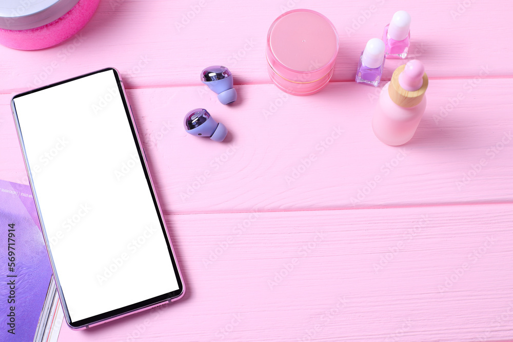 Mobile phone on pink table with headphones on table with cosmetics Mobile phone on pink table with headphones on table with cosmetics