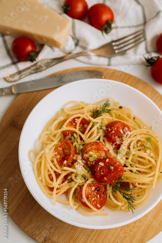 Portion of spaghetti pasta with parmesan and cherry tomatoes sprinkled with spices in a plate on a wooden board