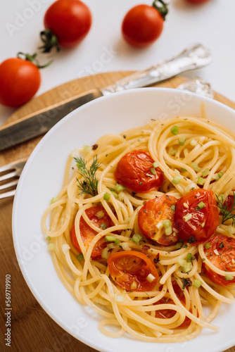 Close up portion of spaghetti pasta with cherry tomatoes sprinkled with spices in a plate on a wooden board