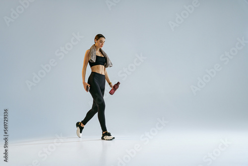 Woman walking with water bottle and towel over studio background . Healthy lifestyle