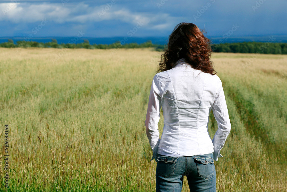 Rear view of young woman overlooking farmland in summer. Rear view of young woman overlooking farmland in summer.