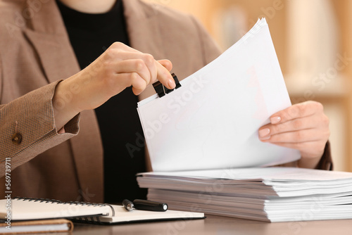 Woman attaching documents with metal binder clip at table in office, closeup