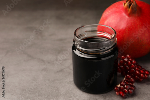 Glass jar of tasty pomegranate sauce and fresh ripe fruit on light grey table. Space for text