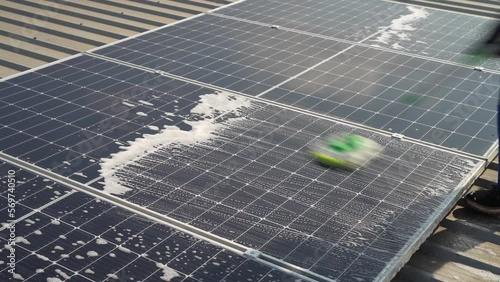 Technician using a mop and water to clean the solar panels that are dirty with dust and birds' droppings to improve the efficiency of solar energy storage.