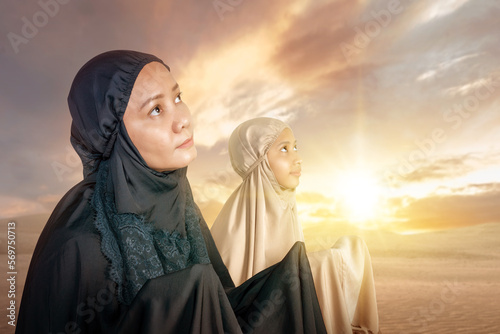 Asian Muslim mother and daughter in a hijab raised hands and praying together photo