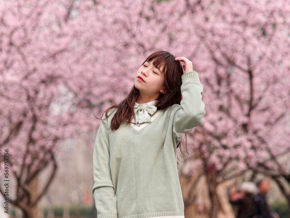 Outdoor portrait of beautiful young Chinese girl in Japanese JK style dress posing with blossom cherry tree brunch background in spring garden, beauty, summer, emotion, expression and people concept.