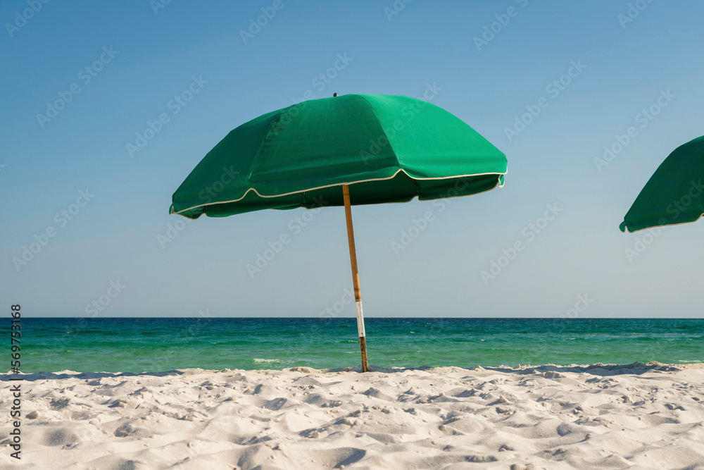 Green umbrella on a white sand at the beach in Destin, Florida. One umbrella against the ocean waves and clear blue skies at the background.