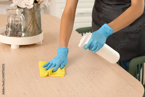 Female janitor cleaning dining table in kitchen, closeup