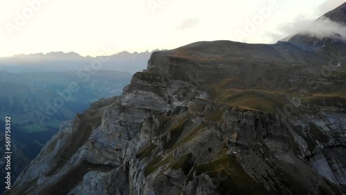 A spinning aerial view of Muttenchopf viewpoint of lake Limmernsee in Glarus, Switzerland, with the Swiss Alps, cliffs, blue water, hikers in view after a sunset photo