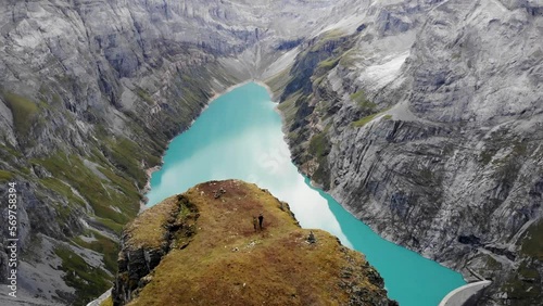 A flyover over hikers walking towards a viewpoint above lake Limmernsee in Glarus, Switzerland, with view of the Swiss Alps cliffs and landscape photo