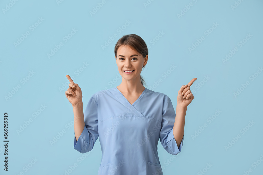 Female medical intern pointing at something on blue background Female medical intern pointing at something on blue background