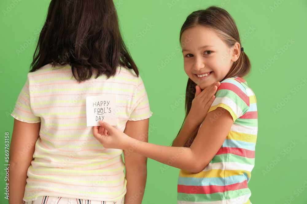 Little girl playing a prank on her sister against green background