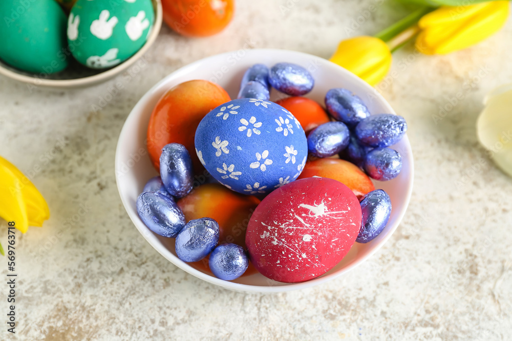 Fototapeta premium Bowl with painted Easter eggs and candies on light table