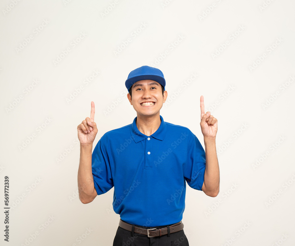 Happy asian man in blue uniform standing on isolated white background. Smiling male delivery service worker pointing the finger to blank space. Delivery courier and shipping service. Happy asian man in blue uniform standing on isolated white background. Smiling male delivery service worker pointing the finger to blank space. Delivery courier and shipping service.