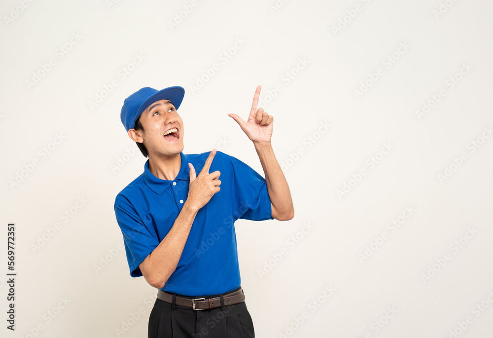 Happy asian man in blue uniform standing on isolated white background. Smiling male delivery service worker pointing the finger to blank space. Delivery courier and shipping service.