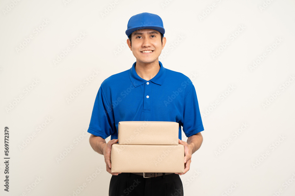 Happy delivery asian man in blue uniform standing holding box parcel cardboard on isolated white background. Smiling male service worker. Delivery courier and shipping service. Happy delivery asian man in blue uniform standing holding box parcel cardboard on isolated white background. Smiling male service worker. Delivery courier and shipping service.