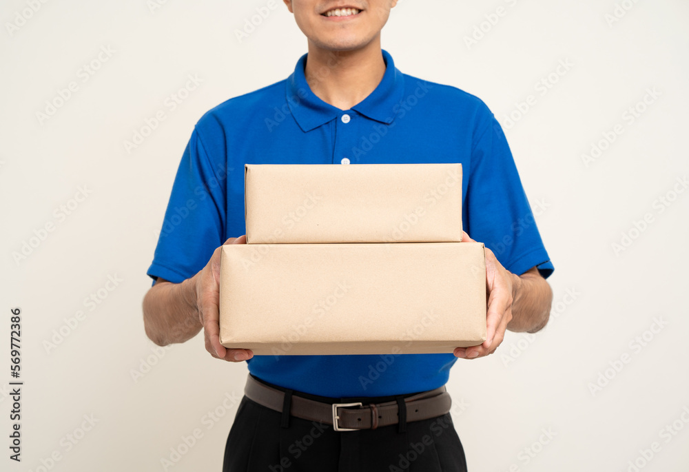 Happy delivery asian man in blue uniform standing holding box parcel cardboard on isolated white background. Smiling male service worker. Delivery courier and shipping service. Happy delivery asian man in blue uniform standing holding box parcel cardboard on isolated white background. Smiling male service worker. Delivery courier and shipping service.
