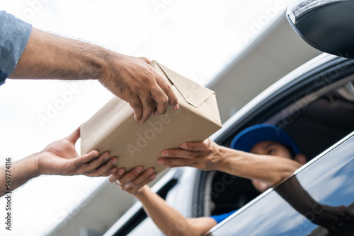 Asian delivery man with parcel in hand of blue uniform sending parcel to customer Sticking his head outta the windshield from shopping online service. Courier man send a package to destination.