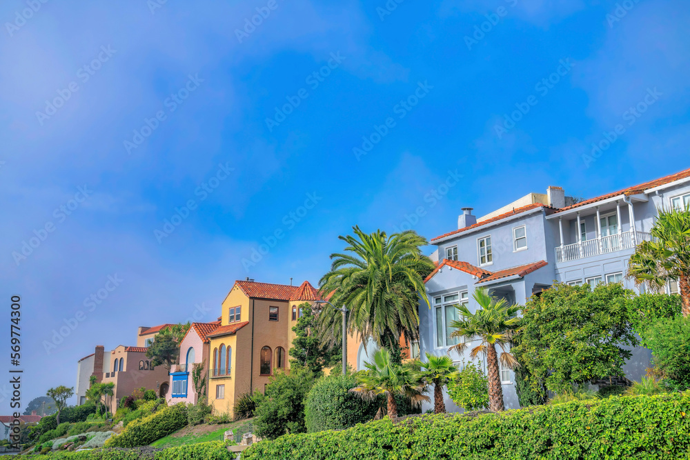 Residential landscape with colorful houses in San Francisco Califronia. Facade of homes in a beautiful neighborhood with vibrant foliage against blue sky.