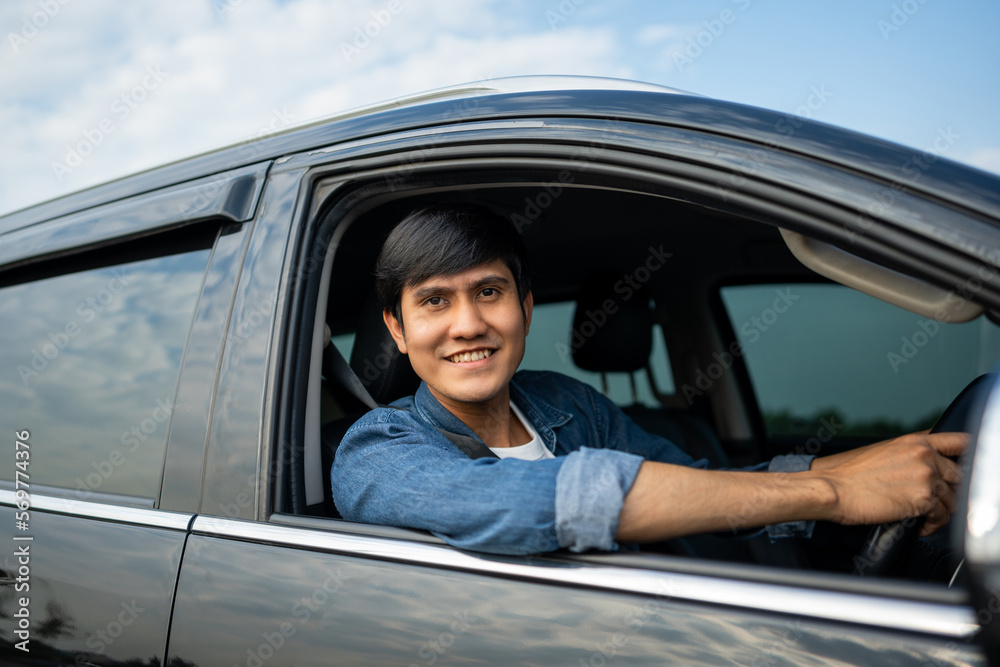 A young Asian man drives a car on a clear day. With beautiful blue sky. He smiling driving to travel by car. Sticking her head outta the windshield A young Asian man drives a car on a clear day. With beautiful blue sky. He smiling driving to travel by car. Sticking her head outta the windshield
