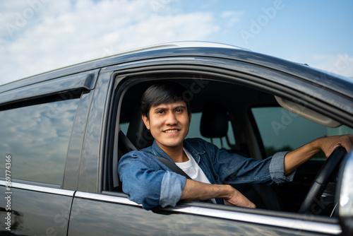A young Asian man drives a car on a clear day. With beautiful blue sky. He smiling driving to travel by car. Sticking her head outta the windshield © Chanakon