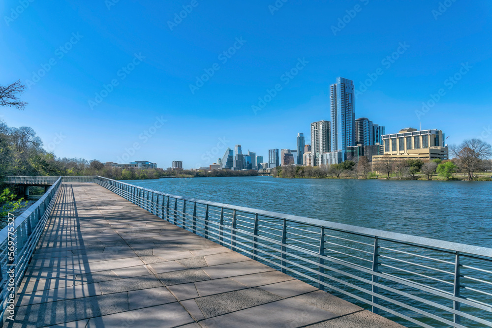 Pedestrian walkway and bike path along Colorado River with luxury apartments. Scenic city and nature landscape in Austin Texas with pathways, water and expensive residential buildings.