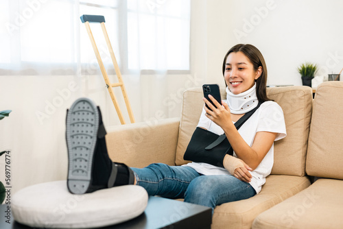 Woman recovery from accident fracture broken bone injury with leg splints in cast neck splints collar arm splints sling support arm using smartphone. Social security and health insurance concept. © Chanakon