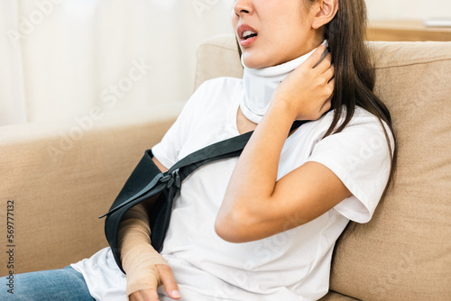 Woman suffered pain from accident fracture broken bone injury with leg splints in cast neck splints collar arm splints sling support arm in living room. Social security and health insurance concept. photo