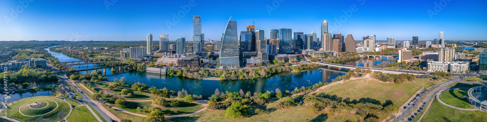 Panoramic view of Colorado River and Austin Texas cityscape. There is a view of a park at the front and bridges over the river near the skyscrapers.